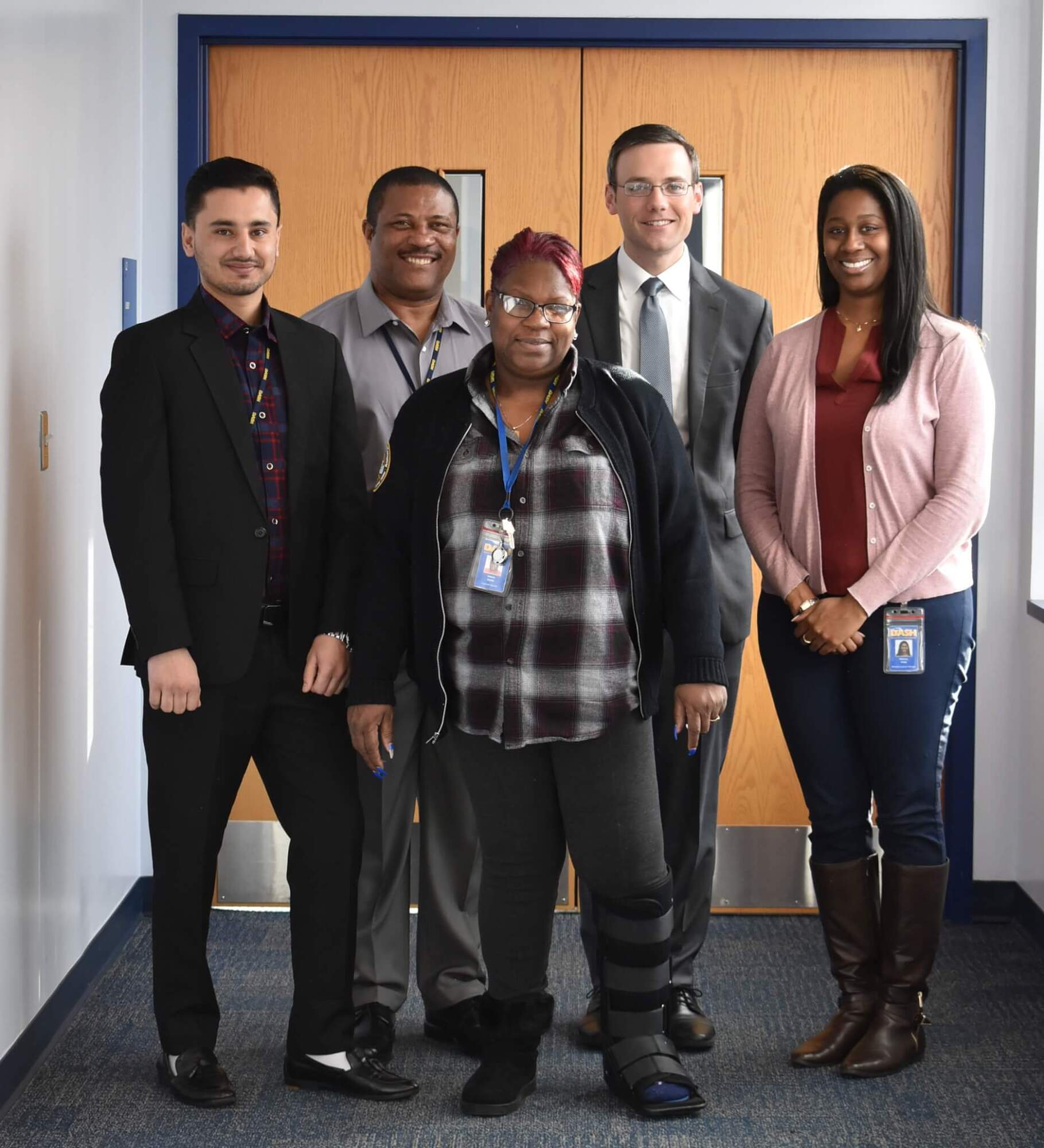 Diverse professional team of five people posing for group photo in office with wooden doors background